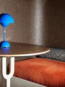 A modern office setup featuring a comfortable couch with a blue desk lamp and a cork wall.