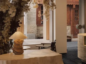A modern restaurant interior featuring wooden chairs and tables on a concrete floor, with a wooden lamp on a concrete table.