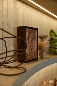 Decorative art piece on a ceramic vase placed on a wooden shelf.