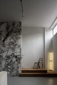 Modern interior design featuring a minimalist room with concrete walls, metal accents, and a single chair on a carpeted step.