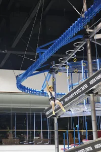 A child is climbing on an industrial-style playground rope course comprised of metal structures and rings.