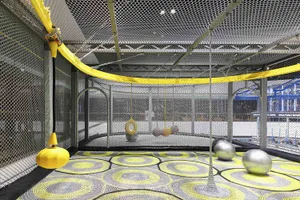 Playground interior with netted walls, metal poles, and suspended balls inside a large, enclosed space with patterned floorin