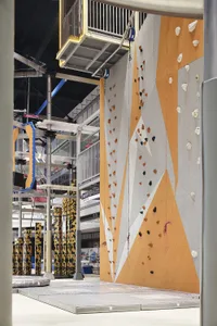 An industrial-style climbing gym with a large climbing wall made of concrete and various climbing holds.