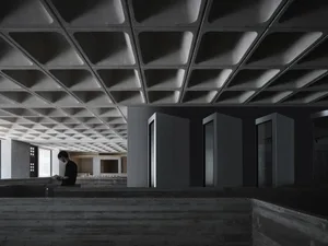 A minimalist office interior featuring concrete walls and a textured ceiling panel.