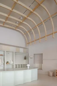 A minimalist clothing shop with a curved wooden counter and exposed wooden beams on the ceiling.
