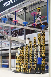Children navigating a 3D-rendered parkour obstacle course on metal columns and platforms.