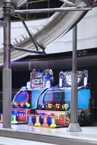 A brightly lit indoor amusement park area with plastic light fixtures and industrial design elements.