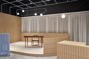 A minimalist restaurant interior with beige tiles and white curtains, featuring a single wooden table and chair on a raised p