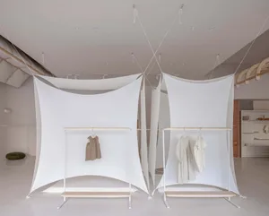 A minimalist retail display featuring white clothing racks with white clothing hung on them, all enclosed by white fabric pan