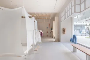 Interior design of a minimalist clothing shop featuring white architectural elements and neutral-colored materials.