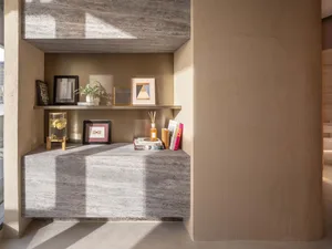 A modern interior space featuring concrete and plaster walls and shelves with framed pictures and books.