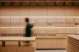 A modern kitchen knife store featuring a wall filled with various knives, wooden shelves, and soft lighting.