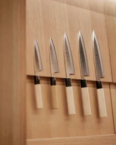 Set of five wooden-handle kitchen knives displayed on a wooden wall background.