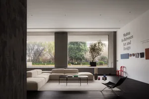 Minimalist living room with concrete walls and furniture, large windows overlooking greenery, and a modern coffee table.