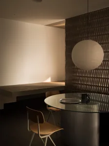 Modern minimalist dining room with glass table and pendant light fixture.