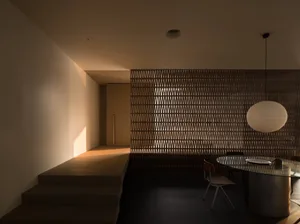 A minimalist dining room with wooden furniture, featuring a round glass table and a light fixture.