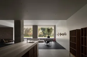 A modern living room with concrete walls and floors, featuring minimalistic furniture and large windows.