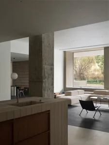 Modern minimalist living room with exposed concrete columns and large windows.