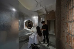 A modern salon featuring a metallic wall and glass counter with a stylist working on a client's hair.