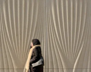 A person walking past a textured metallic facade wall.