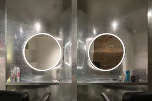 A modern salon interior with metallic glass walls and circular mirrors.