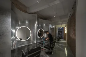 A modern barber shop featuring metallic finishes, industrial lighting, and illuminated circular mirrors.