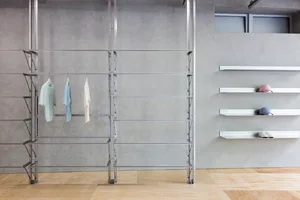 Retail store interior featuring metal shelves with clothes hanging on them against a concrete wall with a wooden floor.