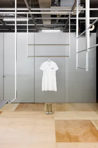 A minimalist fashion display featuring a white dress hanging on a metallic rod against a grey metallic wall, with wooden floo