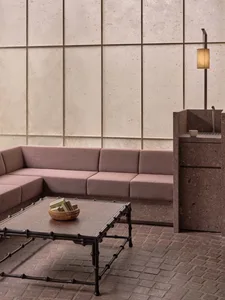 A modern living room with a pink upholstered sofa, a textured table, and a lamp with a paper lampshade.