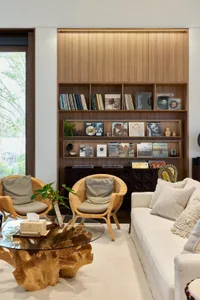 Modern living room featuring a white sofa and two rattan armchairs arranged around a glass coffee table, with a large bookshe