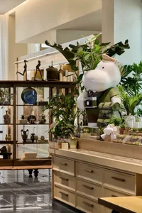A retail shop featuring a mixture of materials and plants, with a large hippo figure holding a camera.