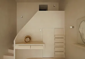 A minimalist white interior space with steps, a desk, and a metallic sculpture.
