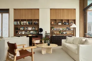 A modern living room with a comfortable sofa, chairs, and wooden shelves displaying books, records, and other decorative item