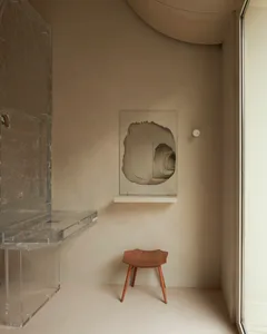 A minimalist interior featuring an acrylic desk and abstract artwork on a muted beige wall.