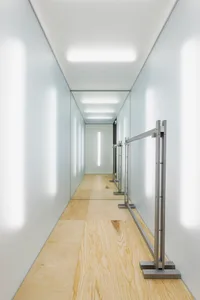 A minimalist corridor with wooden flooring and metallic railings.