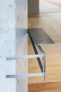 A metal bracket mounted on a concrete wall with a horizontal metal shelf.