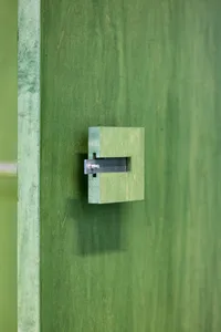 Close-up of a minimalist green door handle mounted on a green wooden door.