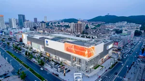 Aerial view of a modern cityscape featuring buildings with glass facades and mixed materials, with mountains in the backgroun