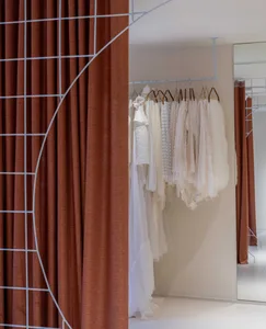 White dresses hanging on a clothes rack in a retail store with white walls and brown curtains.