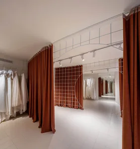 A clothing shop interior with white walls, white floor tiles, and orange curtains.