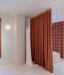 A clothing shop with a white dress hanging on a rail, surrounded by brown curtains.