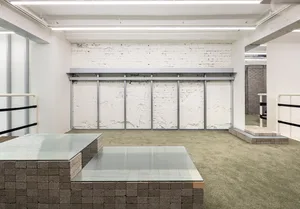 A minimalist installation featuring a concrete structure with glass tables and a green carpet.