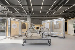 A modern minimalist exhibit showcasing bicycle and clothing products in a clean, industrial-style room with glass and metal d