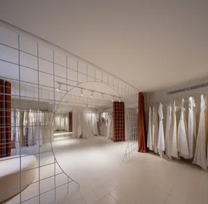A minimalist wedding dress shop featuring a white metal grid structure, white fabric walls, and hanging white dresses with wa