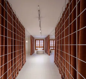 A modern corridor with textile walls and white flooring, featuring seating areas and grid-like structures.