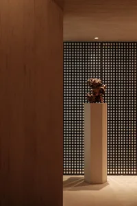 An abstract sculpture displayed on a pedestal within a modern lobby, constructed of concrete material.