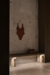Modern minimalist concrete locker room with a brown swimsuit hanging on a hook and towels stacked on a bench.