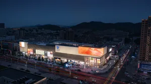 A modern retail shopping center with illuminated metal cladding at dusk.