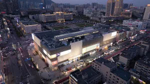 A modern shopping center with a concrete structure, surrounded by street-level stores and a large parking lot.