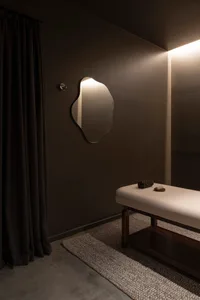 A modern spa interior with a square wall mirror, minimalist black design, and a massage bed.